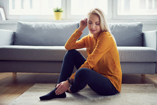 A woman in a yellow sweater, sat on the carpet on the floor in front of her grey couch, all free from infestations of carpet worms.