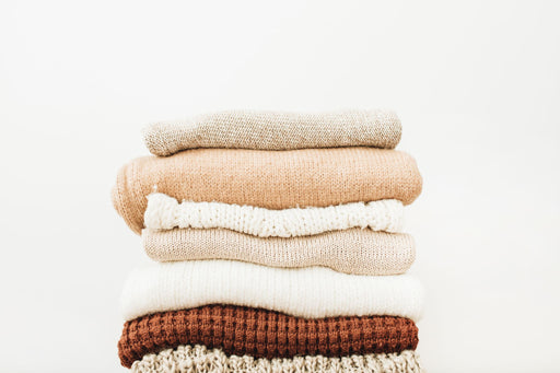 a pile of sweaters in brown and cream colors.