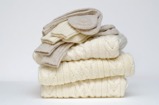 folded pile of  cream woolens with socks on the top of them
