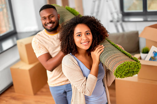 a young couple moving into their new property carrying a roll of carpet