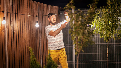 a man fixing up lights in his garden at night