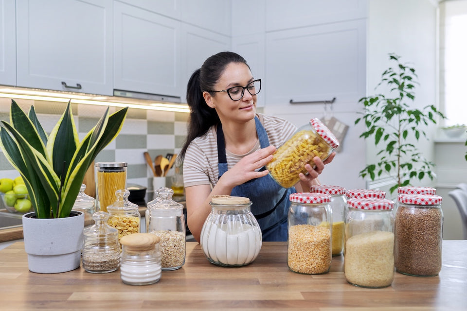 a woman storing her rice, pasta and dry goods in glass containers with lids
