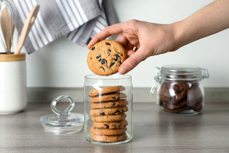a hand taking a cookie out of a glass cookie jar with a lid