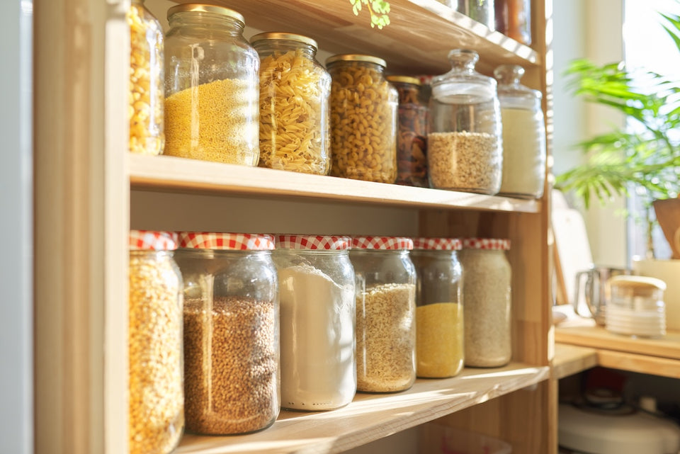 rows of glass jars full of seeds, dried beans and pasta on a pantry shelf