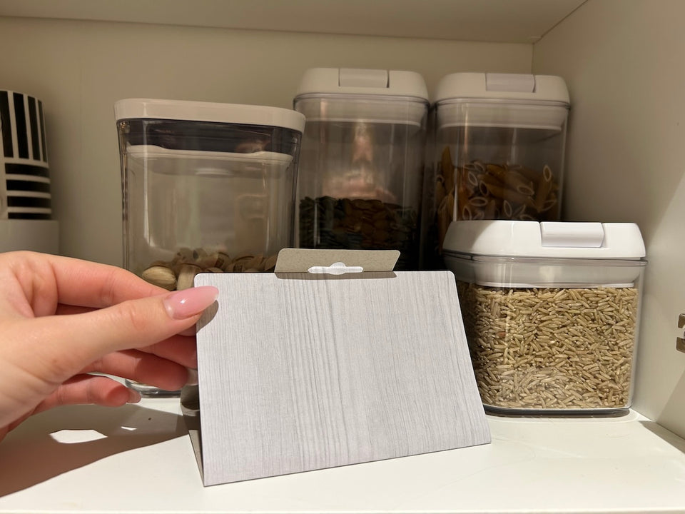 a Pantry Moth Trap being placed on a shelf next to rice and pasta dry food stuffs in sealed containers