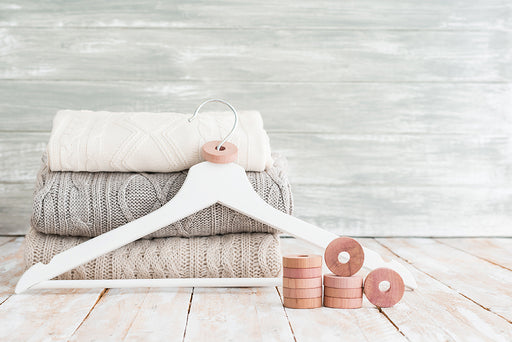 a pile of sweaters next to some cedar rings which are placed over the hook of a hanger