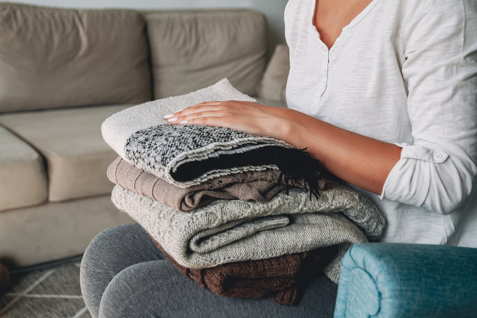 a close of up a pile of jumpers that a woman is holding while sitting down