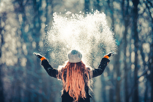 the back view of a woman with long hair, throwing snow in the air on a cold winter day